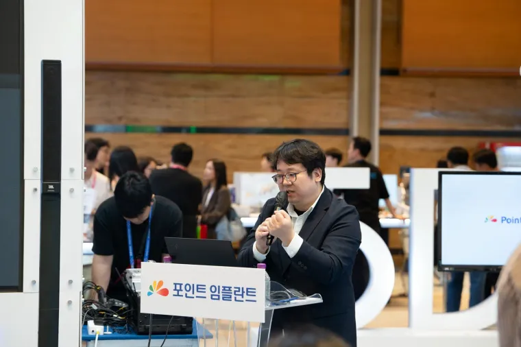 포인트 임플란트 부스 연단에서 마이크를 잡고 강연하는 김교락 대표원장